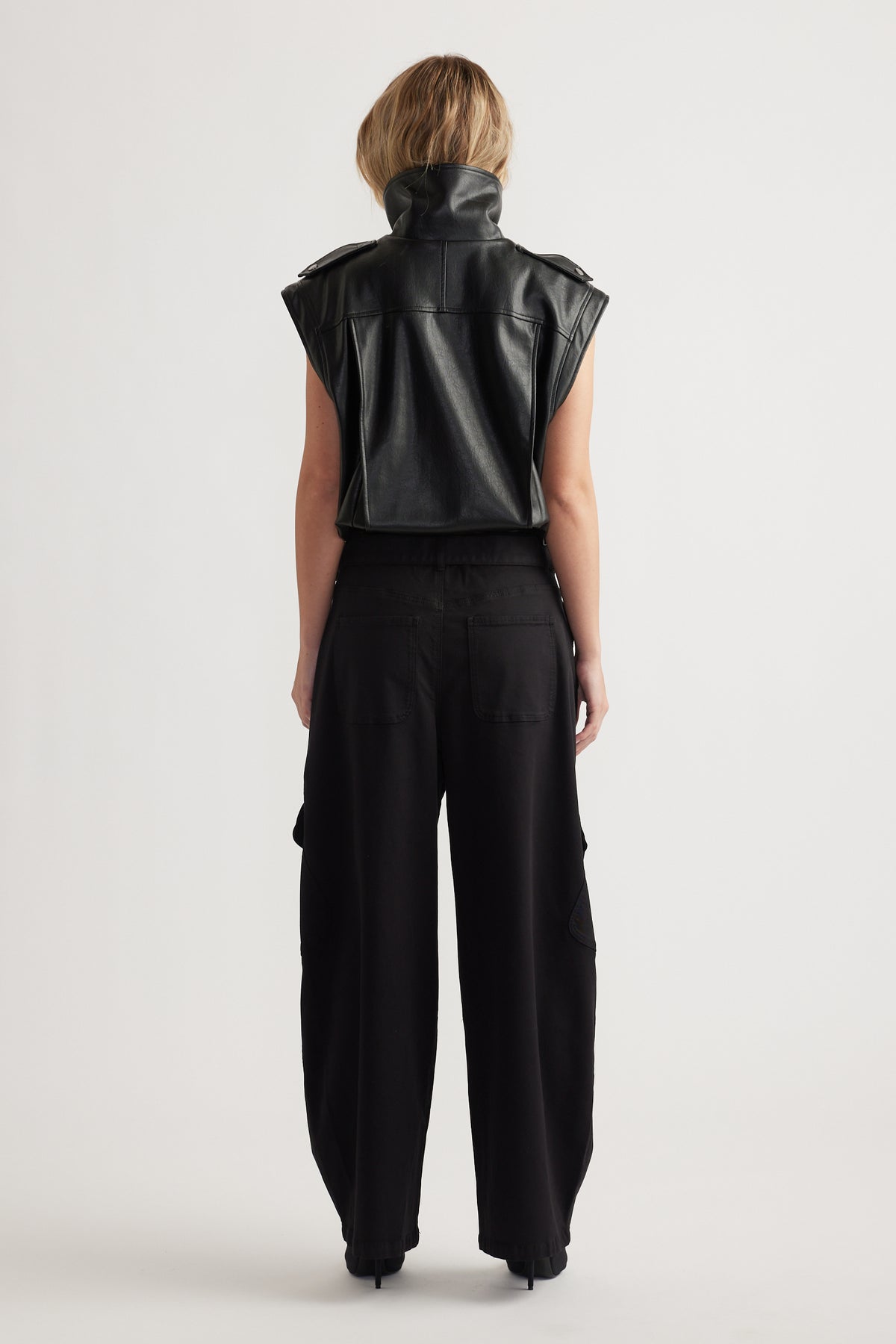 Woman seen from behind wearing a sleeveless black leather top paired with loose black balloon cargo pants and black heels