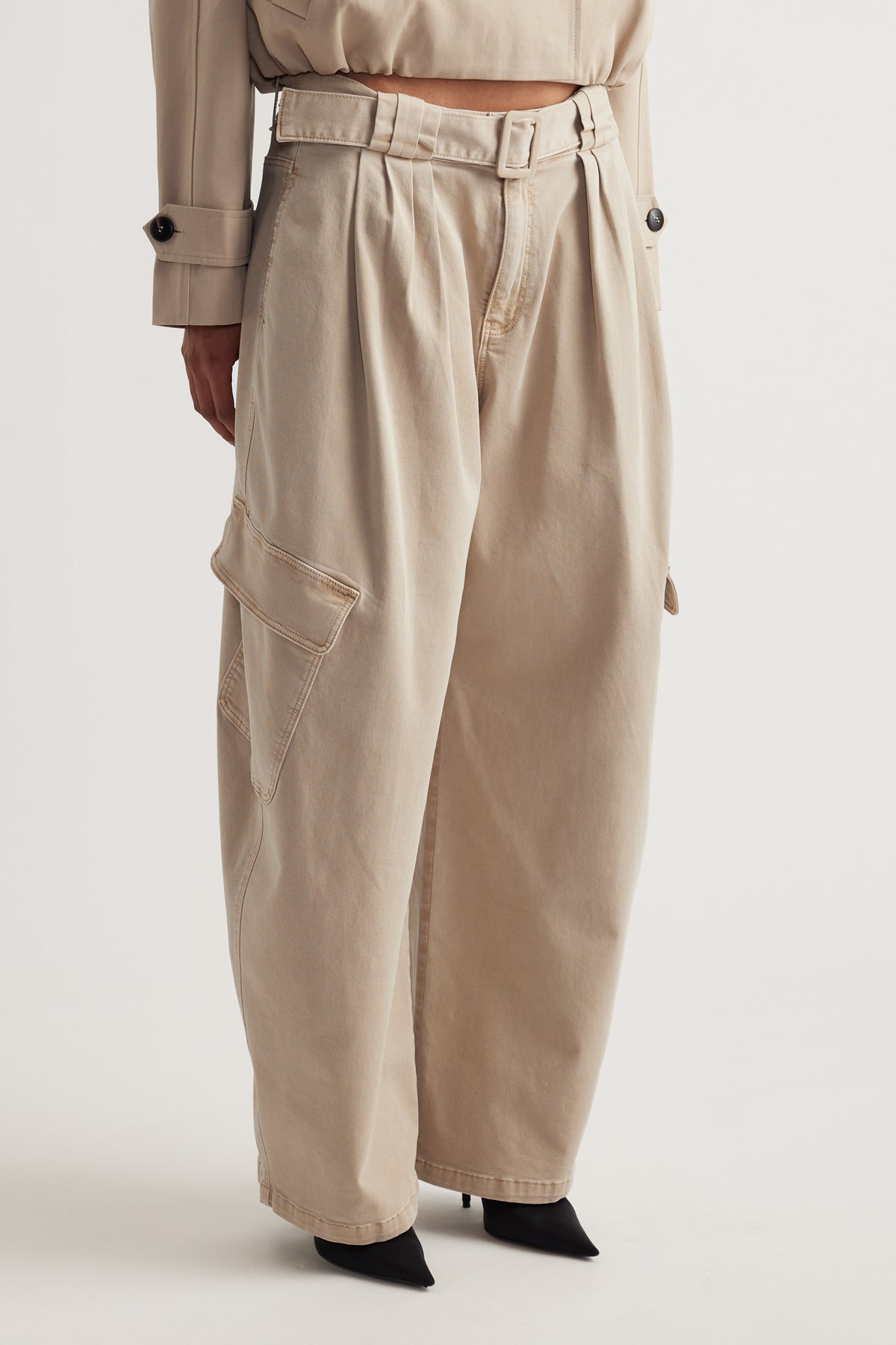 Wide-leg beige balloon cargo pants with a belted waist and flap pockets paired with black pointed heels