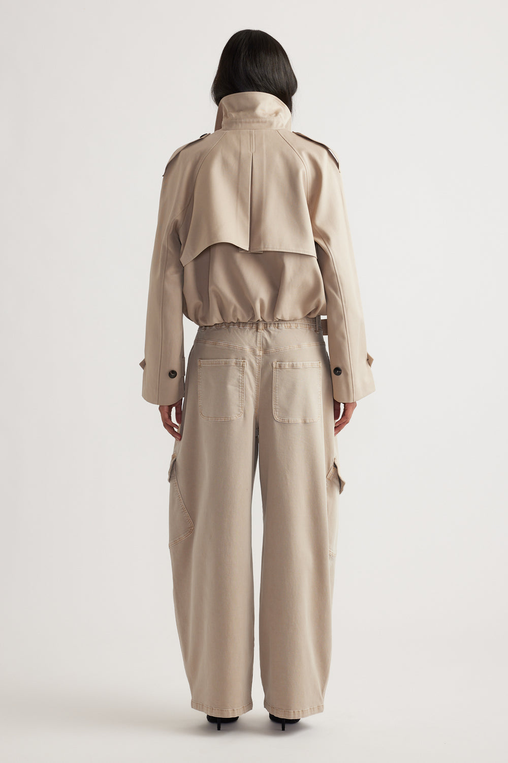 Woman wearing high-waisted wide-leg cargo pants in a neutral tone paired with a cropped trench jacket, shown from behind
