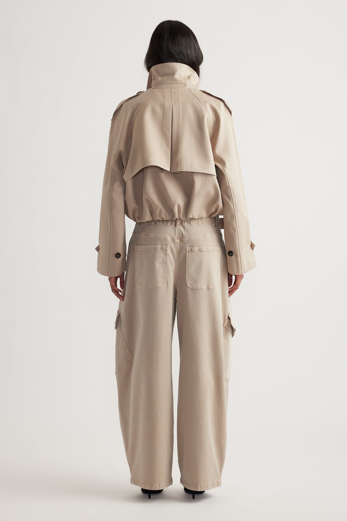 Woman wearing high-waisted wide-leg cargo pants in a neutral tone paired with a cropped trench jacket, shown from behind