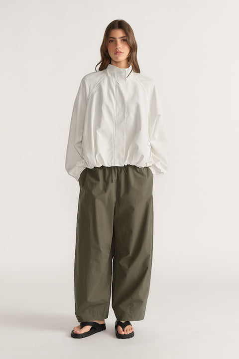 Woman wearing a white high neck blouse with olive barrel leg pants and black sandals