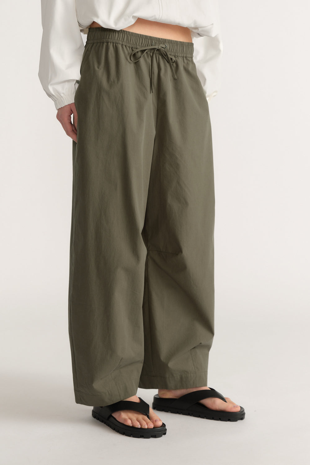 Woman wearing olive green barrel leg pants with an elastic waist, white top and black sandals