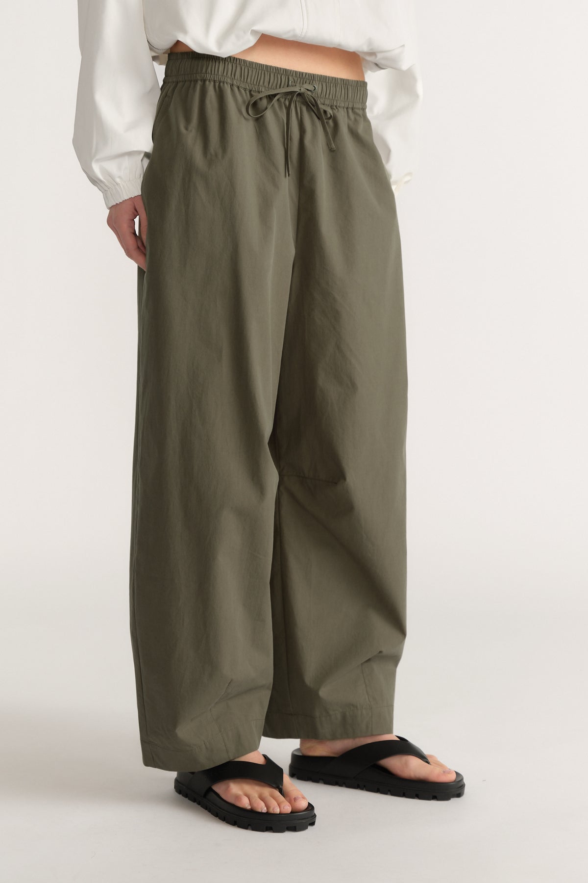 Woman wearing olive green barrel leg pants with an elastic waist, white top and black sandals