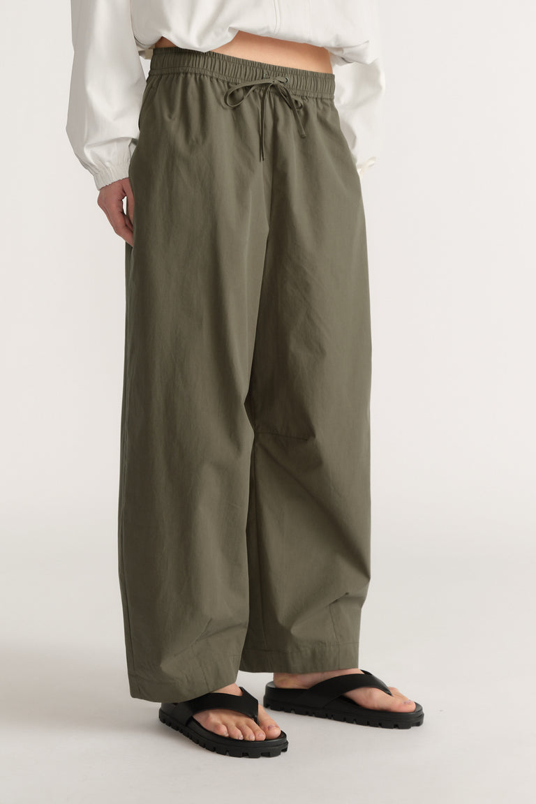 Woman wearing olive green barrel leg pants with an elastic waist, white top and black sandals