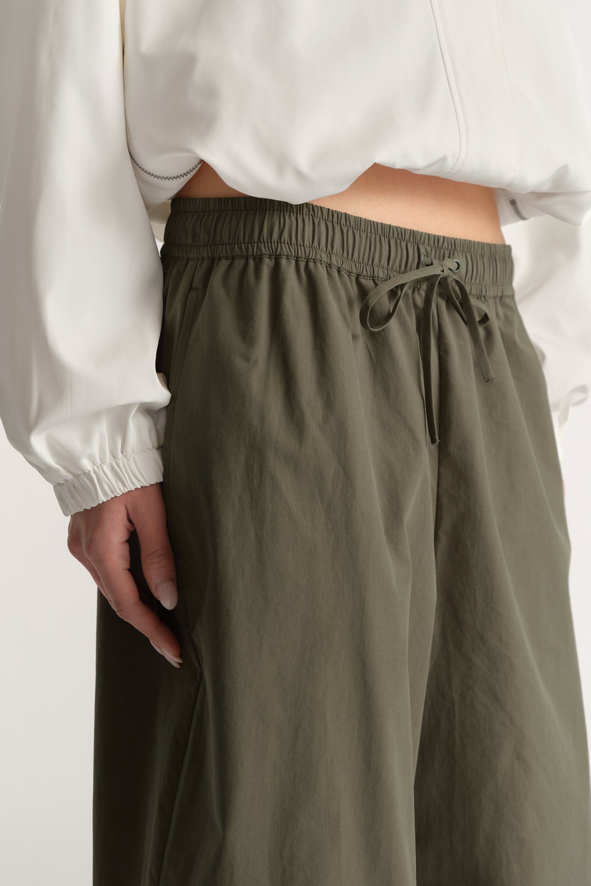 Woman wearing olive barrel leg pants with an elastic drawstring waist and a white cropped sweatshirt