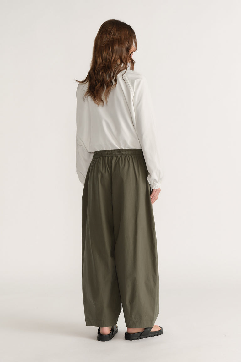 Model in a white long sleeve top, olive green barrel leg pants and black sandals