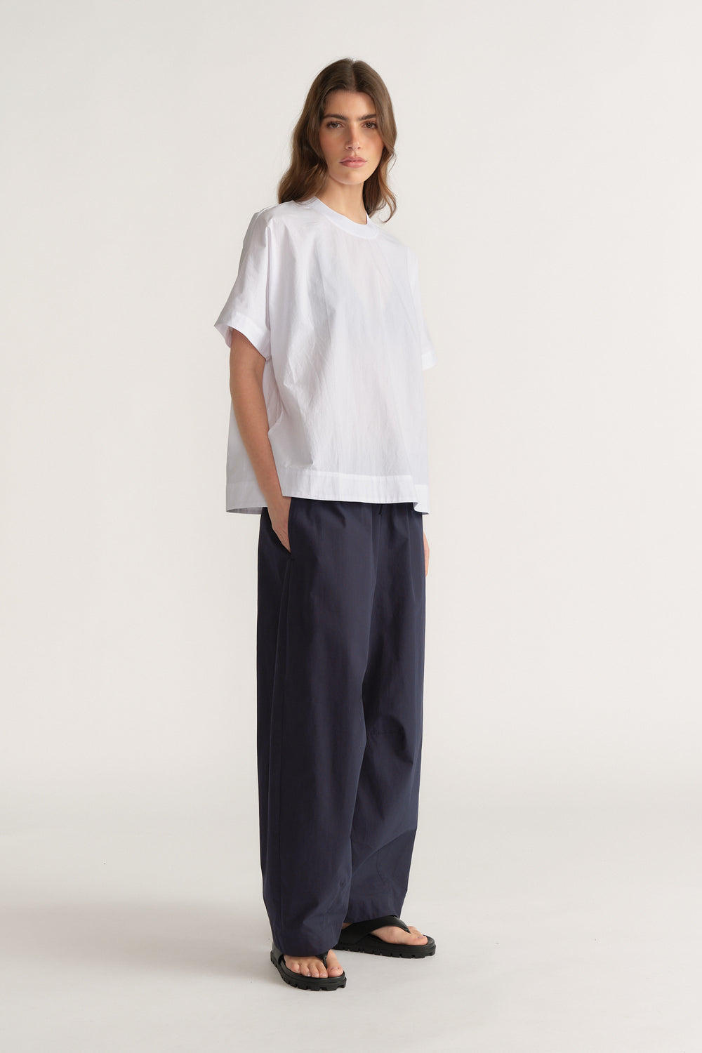 Model wearing a white oversized T shirt with dark navy barrel leg pants and black sandals