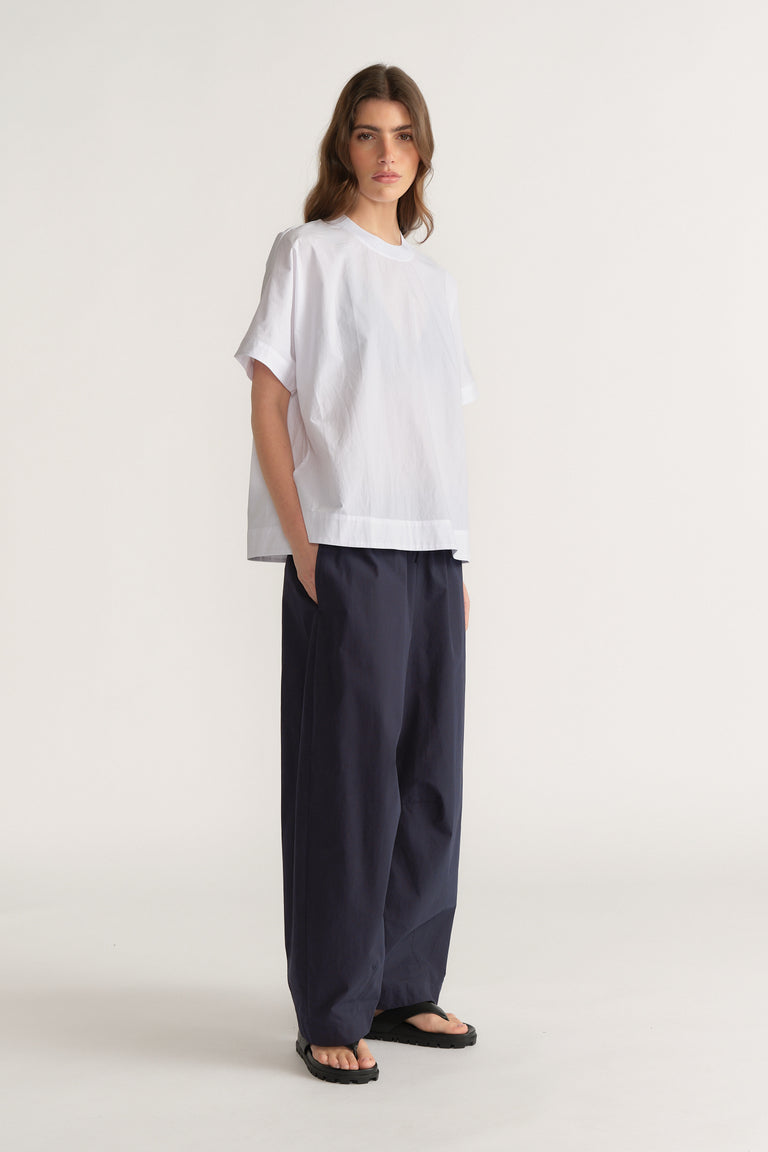 Model wearing a white oversized T shirt with dark navy barrel leg pants and black sandals