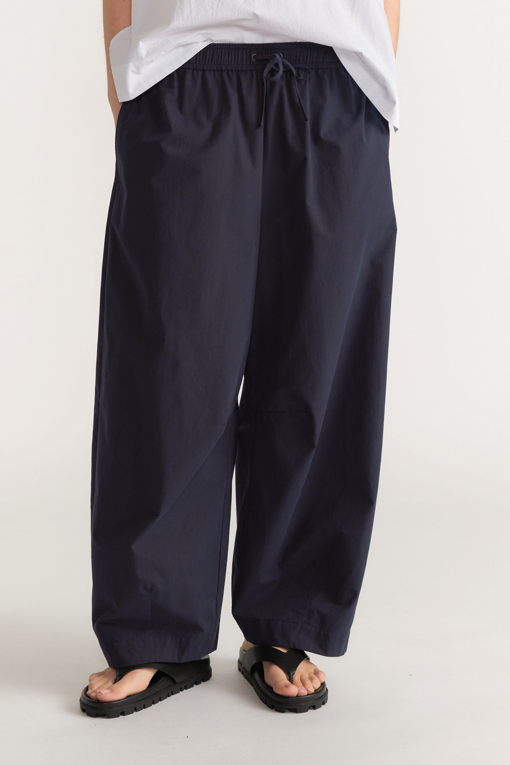 Woman wearing navy barrel leg pants with an elastic drawstring waist, white tee and black sandals