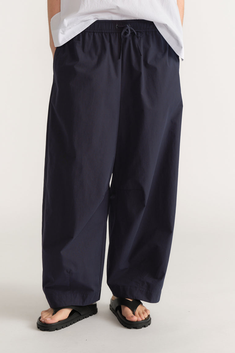 Woman wearing navy barrel leg pants with an elastic drawstring waist, white tee and black sandals