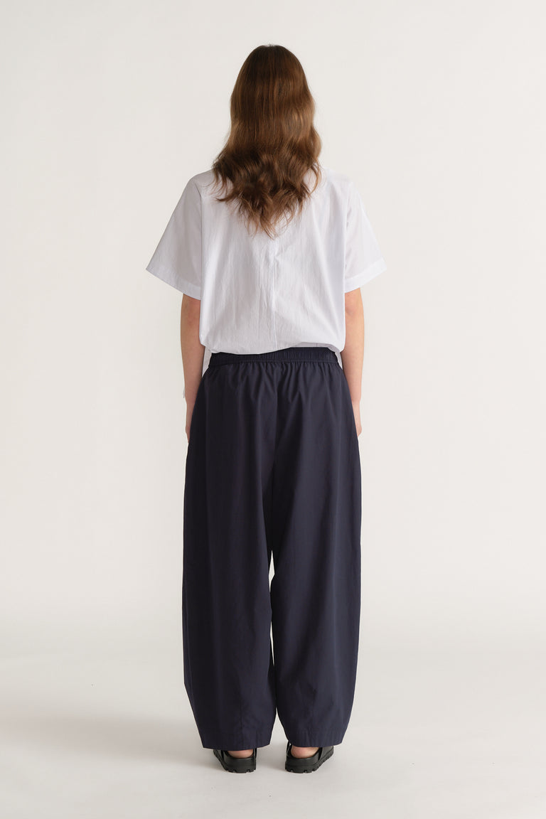 Woman wearing a white short sleeve top with navy barrel leg pants and black shoes, viewed from behind