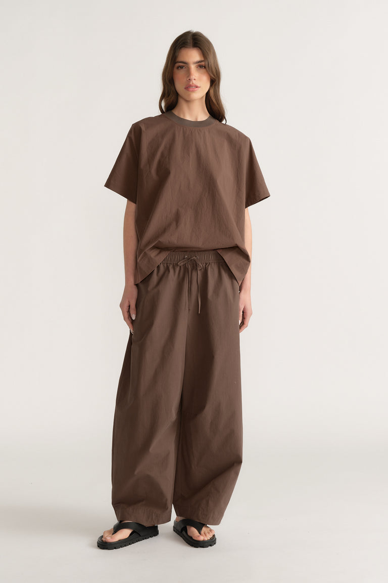 Woman wearing brown barrel leg pants with a matching relaxed tee and black sandals