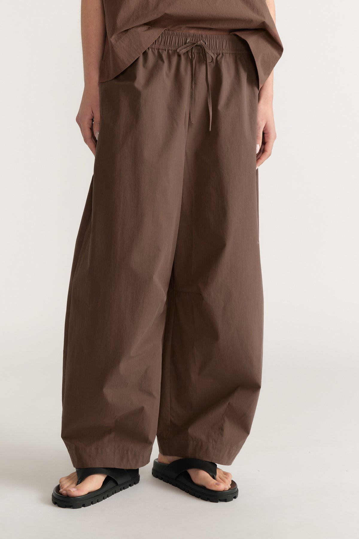 Woman wearing brown elastic waist barrel leg pants with a matching top and black sandals