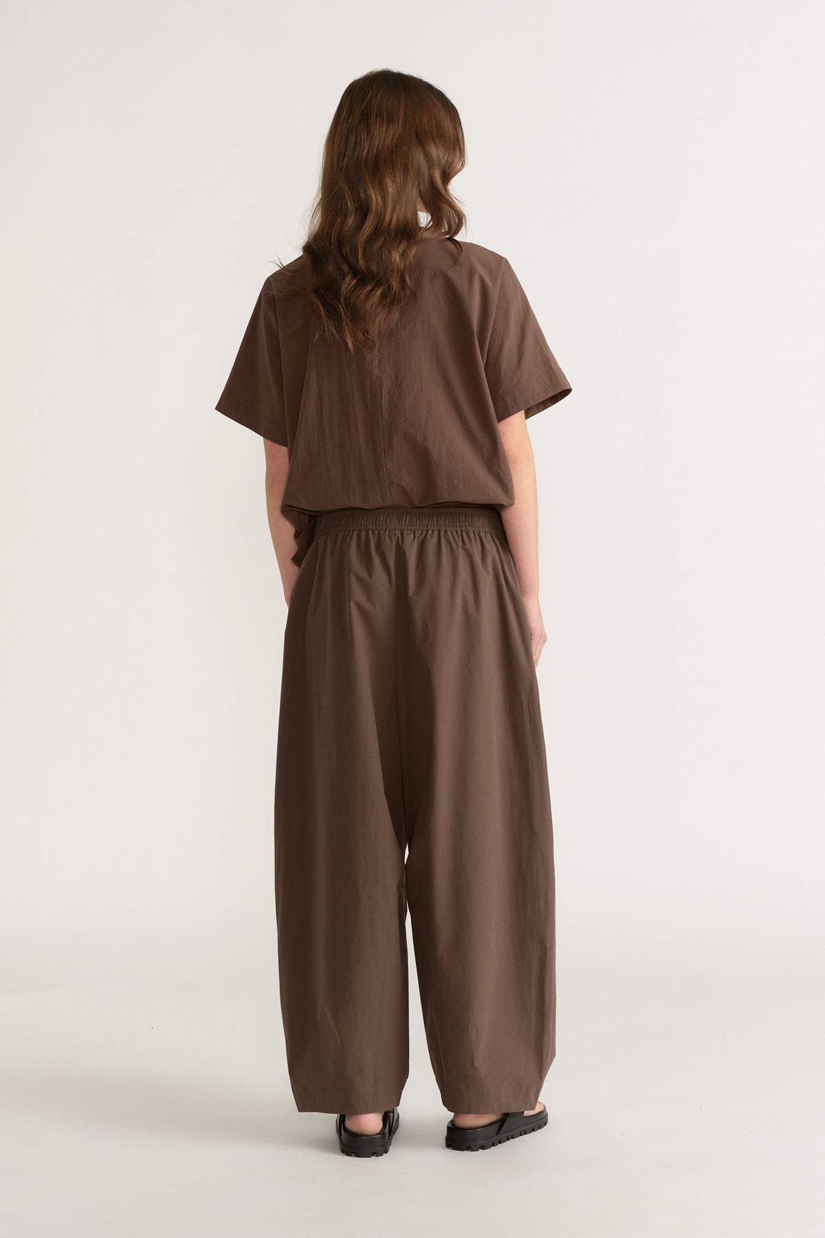 Woman wearing brown barrel leg pants with an elastic waist and matching cropped top with black shoes