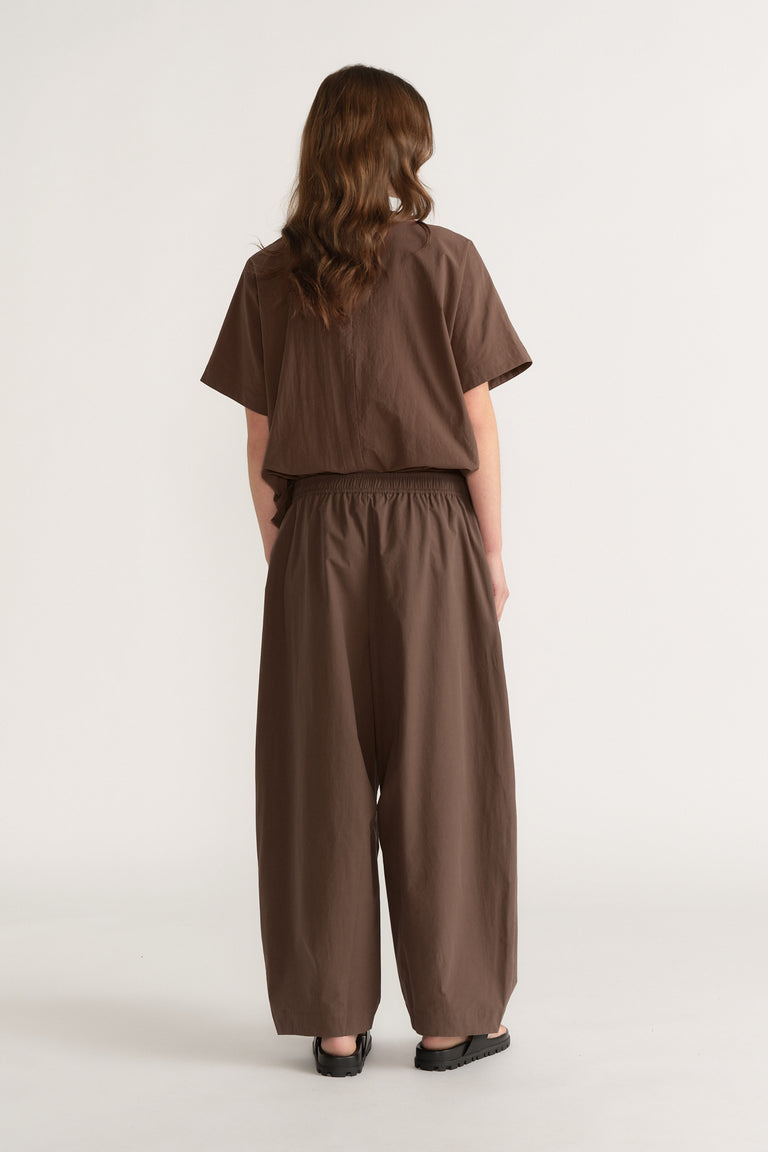 Woman wearing brown barrel leg pants with an elastic waist and matching cropped top with black shoes