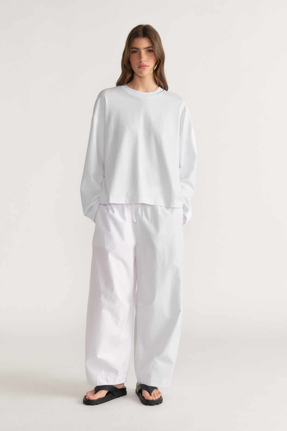 Woman wearing a white long sleeve top with white barrel leg pants and black sandals