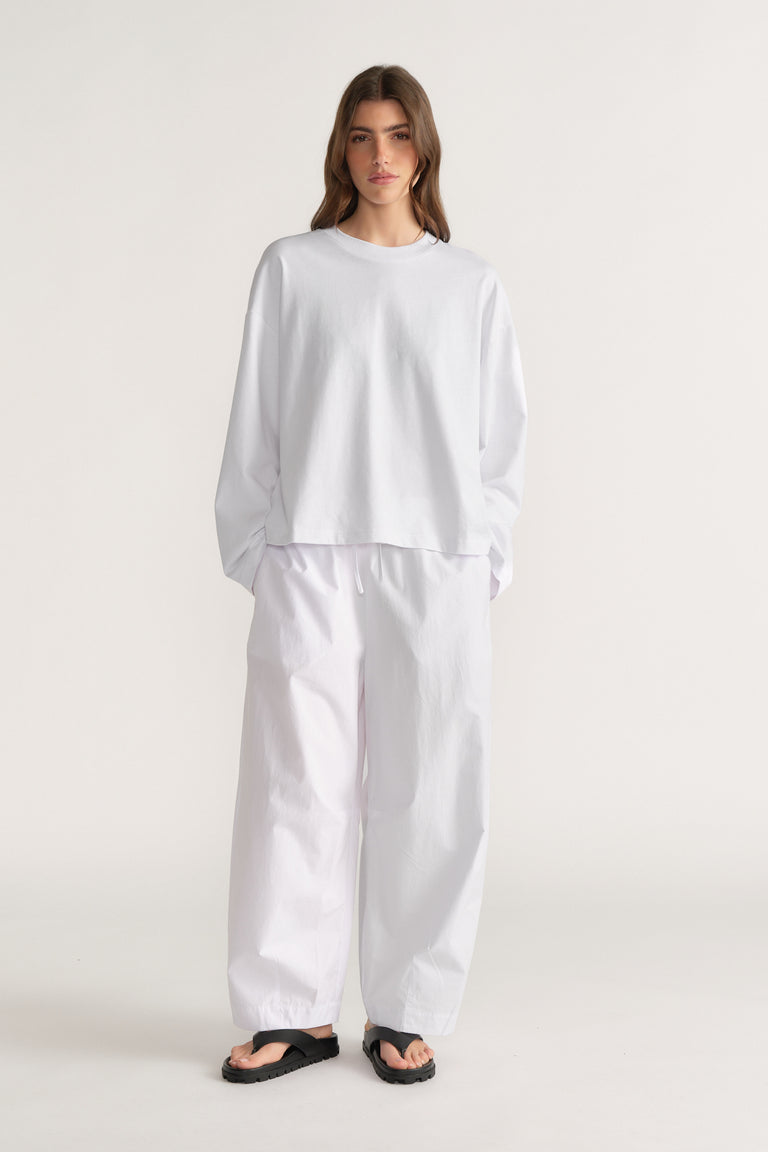 Woman wearing a white long sleeve top with white barrel leg pants and black sandals