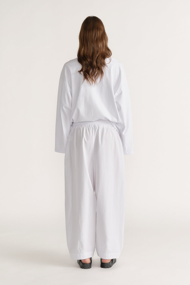Woman viewed from behind wearing a white long sleeve shirt and relaxed barrel leg pants