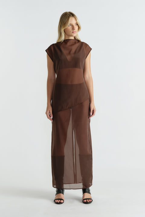 Woman wearing a sleeveless brown sheer dress with an asymmetric hem and black open-toe heeled sandals