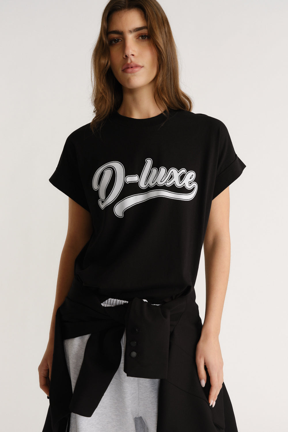 Woman wearing a relaxed black tee with bold "D-luxe" script, styled casually with a tied jacket at the waist.