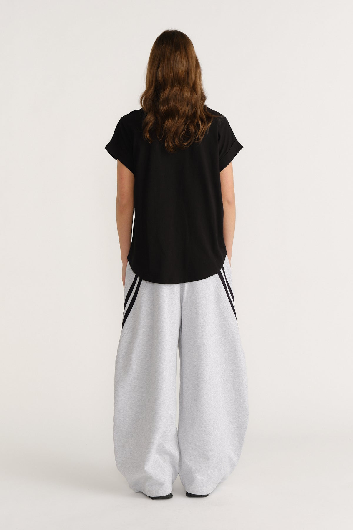 Woman wearing a relaxed black tee paired with wide-leg light grey pants featuring contrasting side stripes.