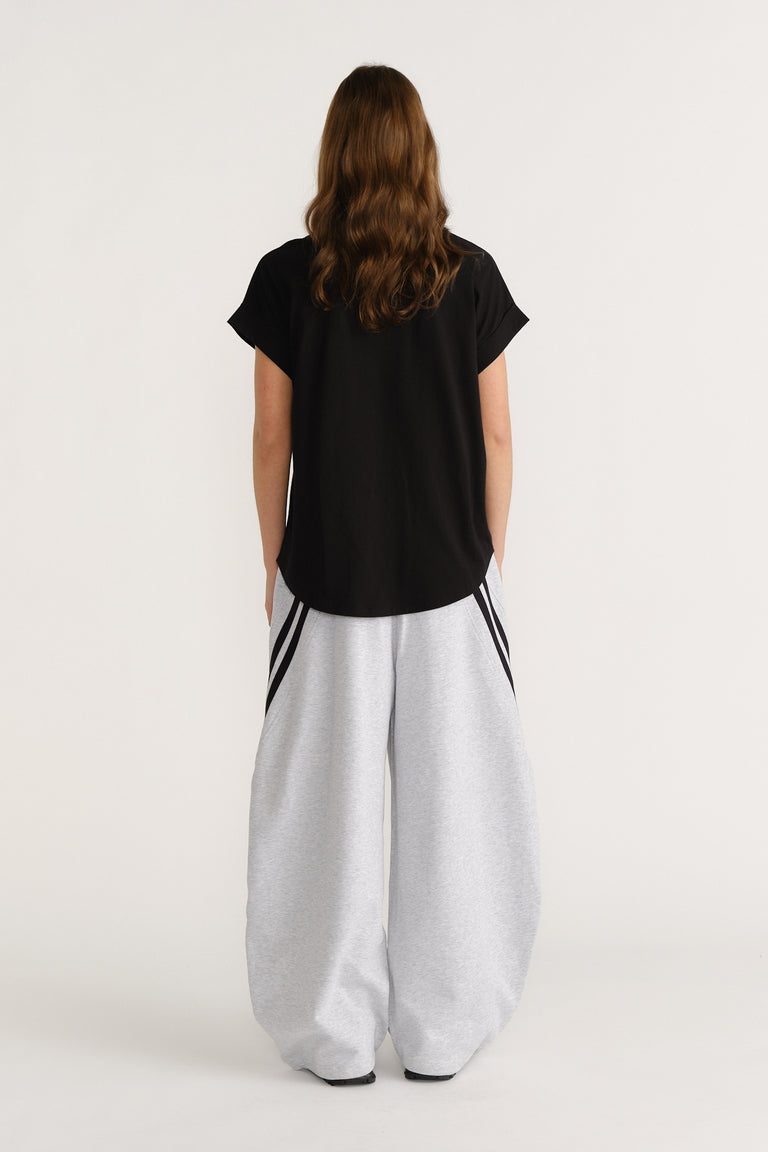 Woman wearing a relaxed black tee paired with wide-leg light grey pants featuring contrasting side stripes.