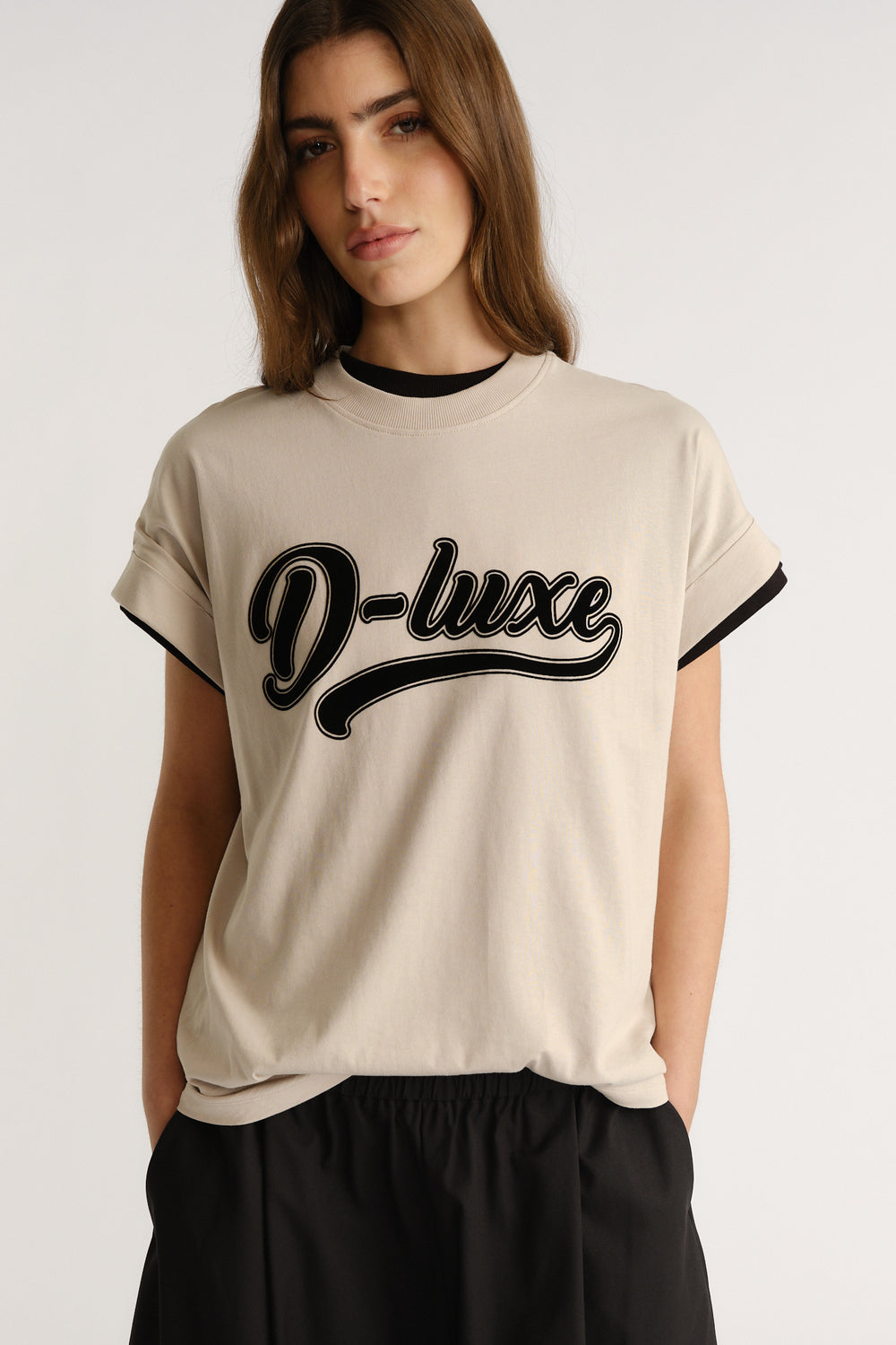 Woman wearing a beige casual tee with bold black "D-luxe" script paired with relaxed black pants for an everyday look