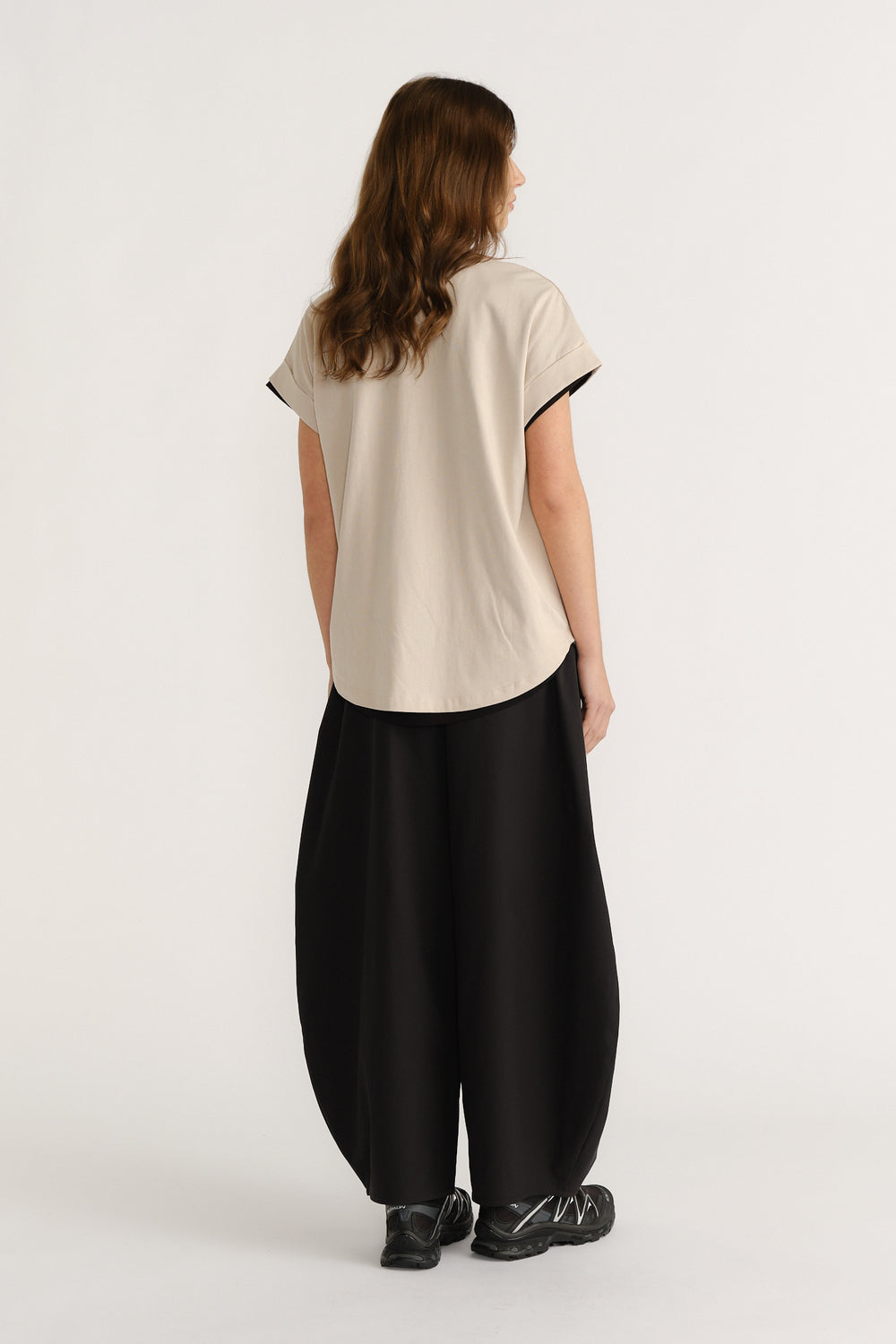 Woman wearing a relaxed beige tee and wide black pants with chunky sneakers, showcasing a casual, modern silhouette.