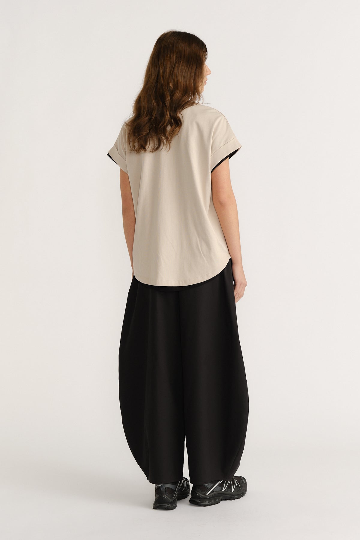 Woman wearing a relaxed beige tee and wide black pants with chunky sneakers, showcasing a casual, modern silhouette.