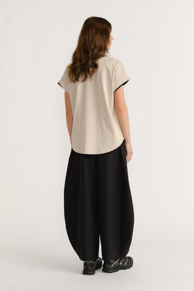 Woman wearing a relaxed beige tee and wide black pants with chunky sneakers, showcasing a casual, modern silhouette.