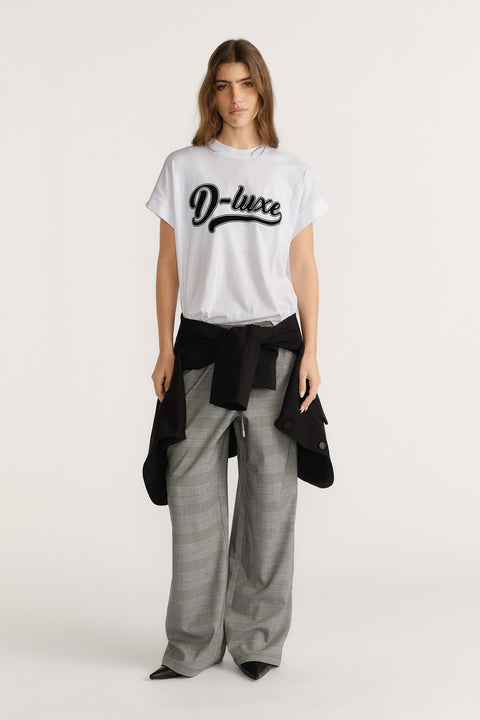 Woman wearing a white graphic tee paired with grey plaid wide-leg pants and a black jacket tied around the waist