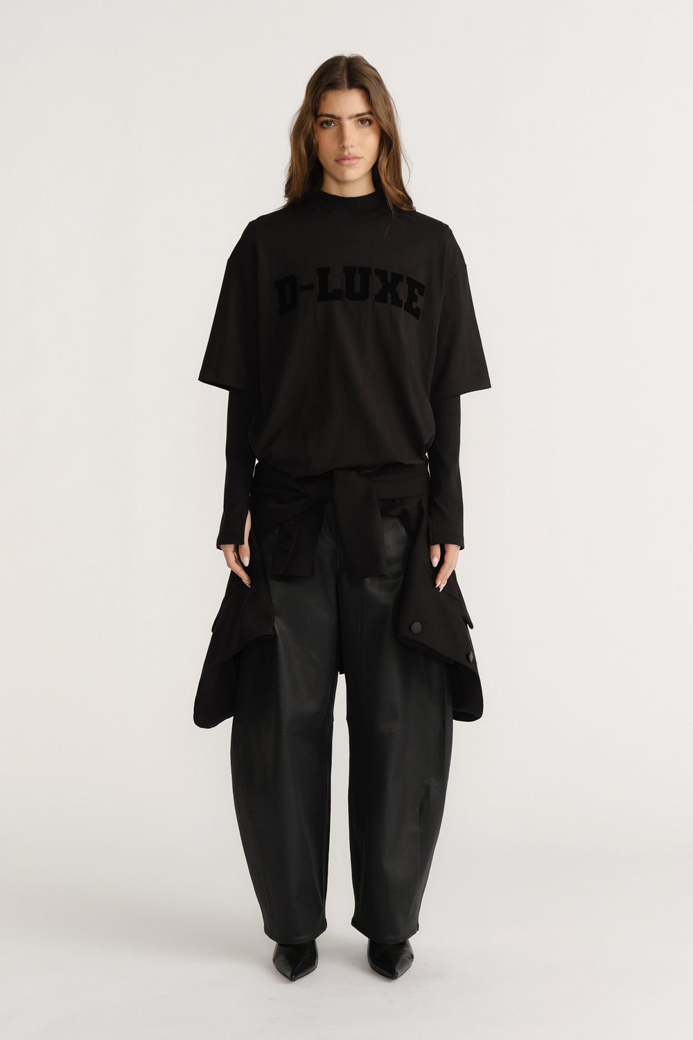 Woman wearing layered black tees with flocked logo detail paired with wide-leg black pants and pointed boots.