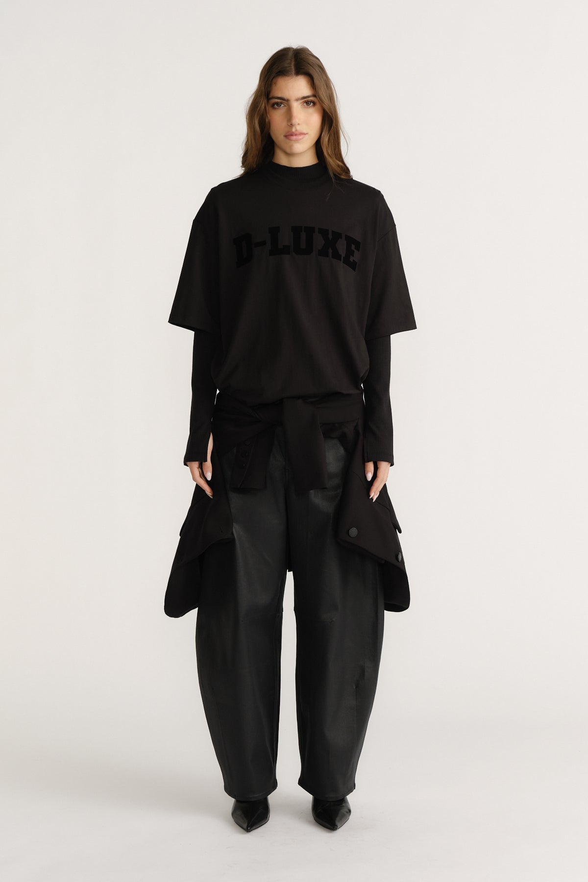 Woman wearing layered black tees with flocked logo detail paired with wide-leg black pants and pointed boots.