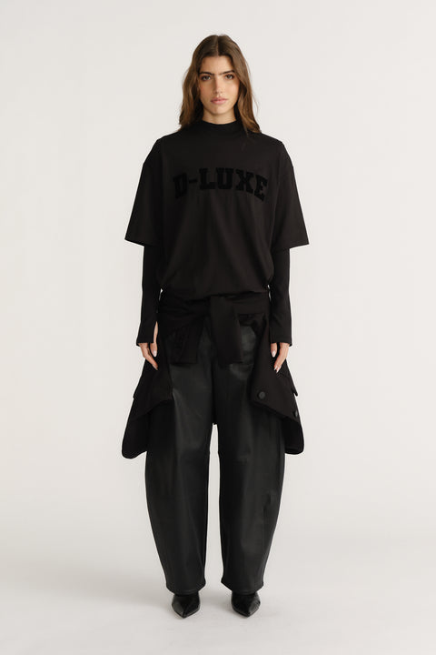 Woman wearing layered black tees with flocked logo detail paired with wide-leg black pants and pointed boots.