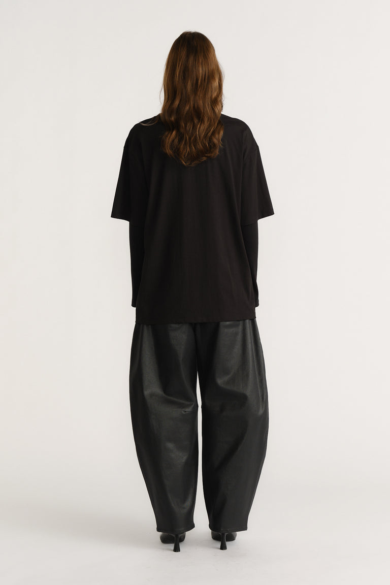 Back view of a woman wearing an oversized black tee paired with wide-leg black pants and black heeled shoes.