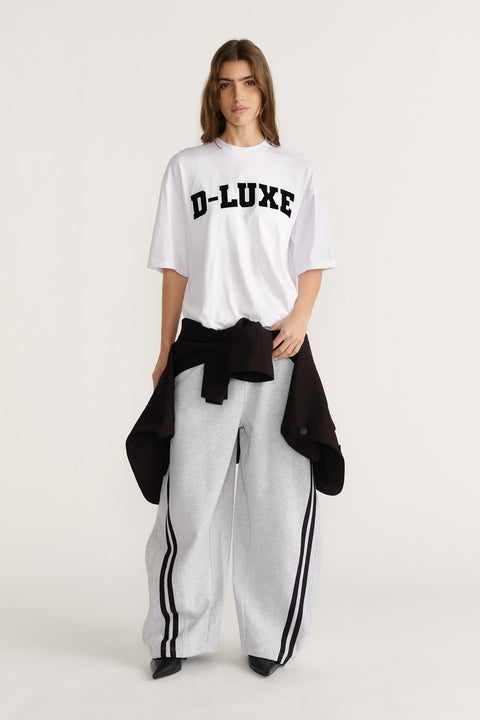 Woman wearing a white relaxed-fit tee with bold black text paired with wide-leg grey track pants with black stripes.