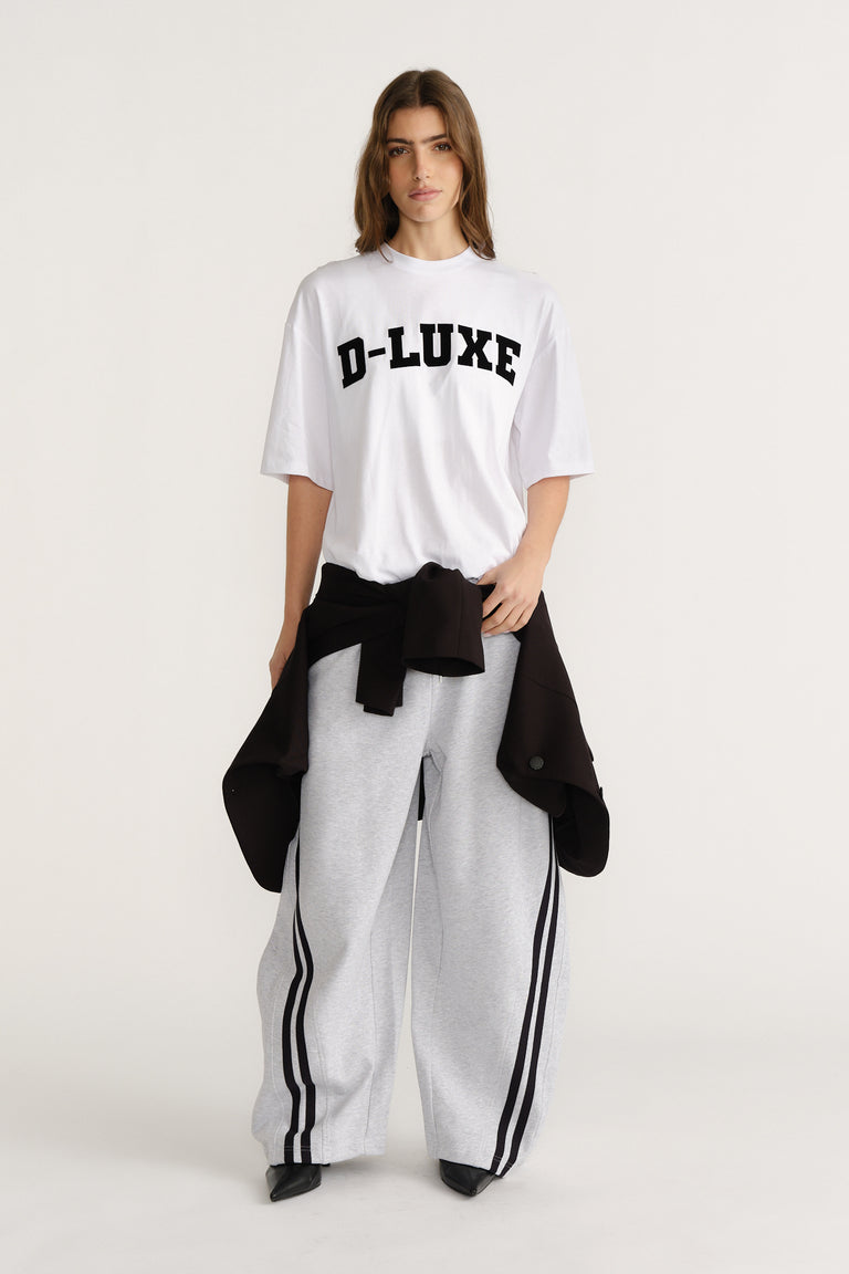 Woman wearing a white relaxed-fit tee with bold black text paired with wide-leg grey track pants with black stripes.