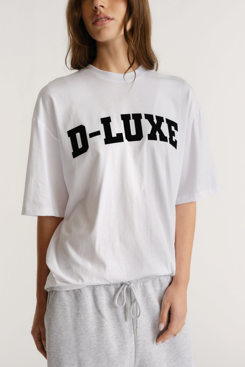 Woman wearing a relaxed white tee with bold black flocked lettering paired with casual light grey drawstring pants.