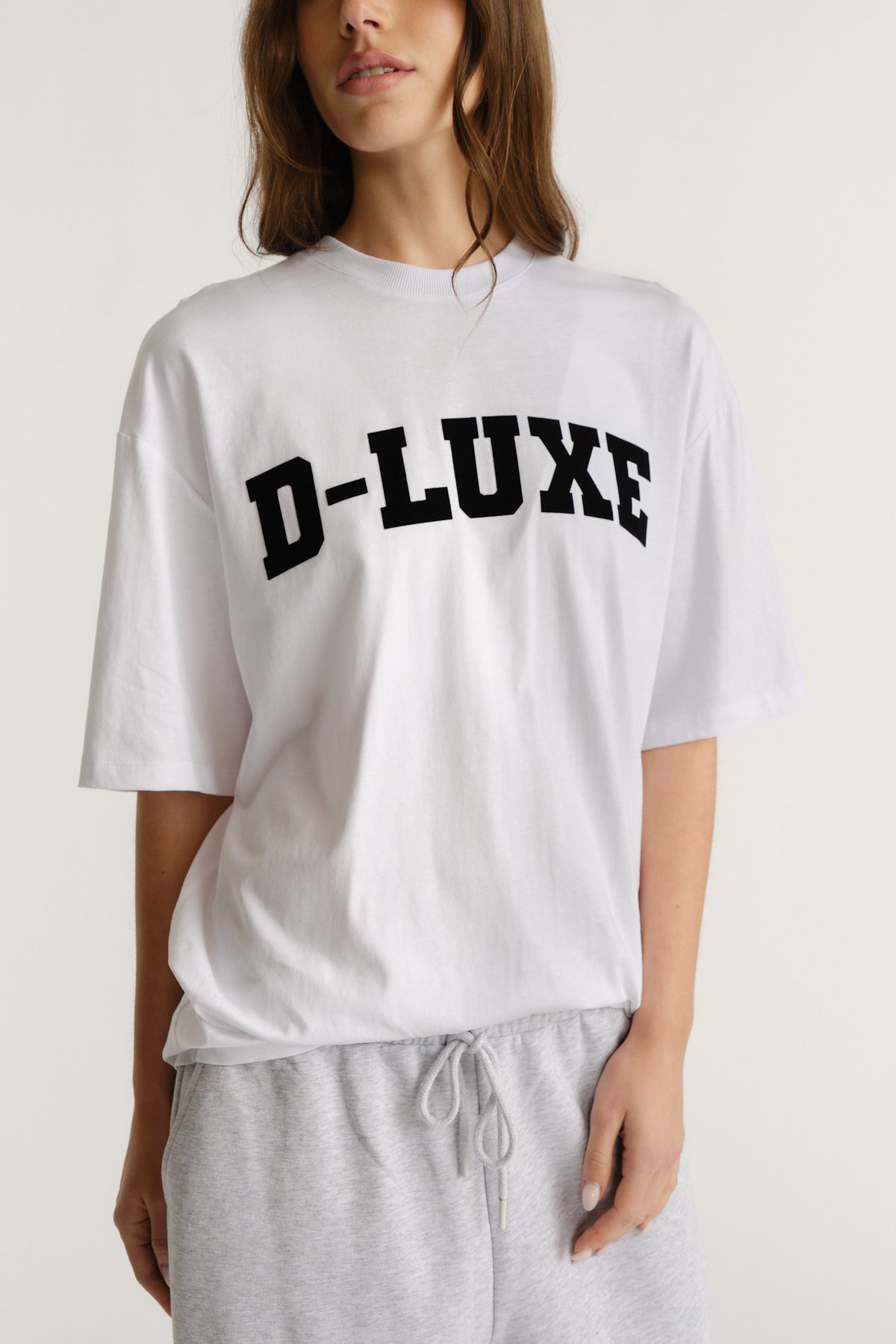 Woman wearing a relaxed white tee with bold black flocked lettering paired with casual light grey drawstring pants.