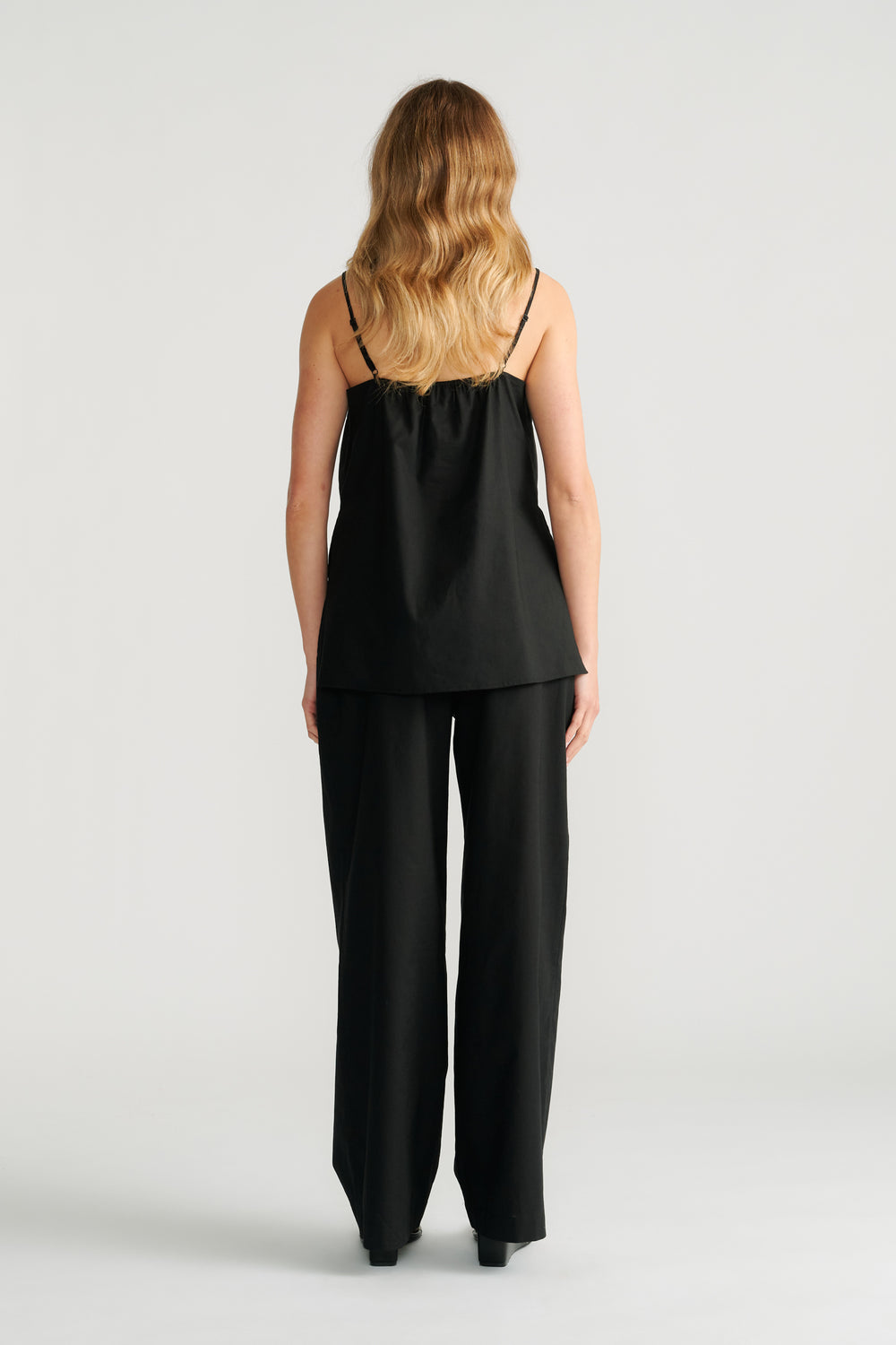 Woman wearing a black cami with thin straps paired with wide-leg black pants, shown from the back.