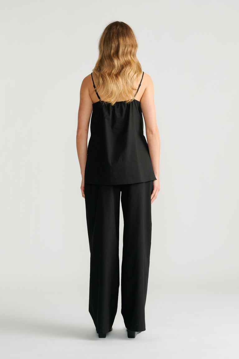 Woman wearing a black cami with thin straps paired with wide-leg black pants, shown from the back.