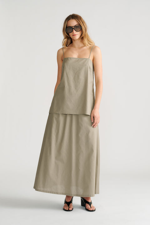 Woman wearing a sage green sleeveless cami layered over a matching long skirt with black heeled sandals and sunglasses.