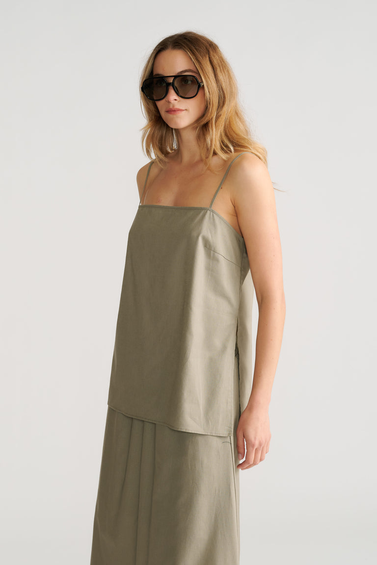 Woman wearing a minimalist sage-green cami top with thin straps paired with a matching flowy skirt and oversized sunglasses.