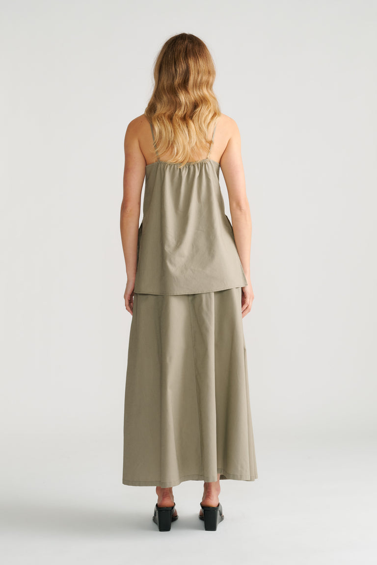 Woman wearing a loose sage green cami with thin straps paired with a matching flowy maxi skirt and black heels, back view.