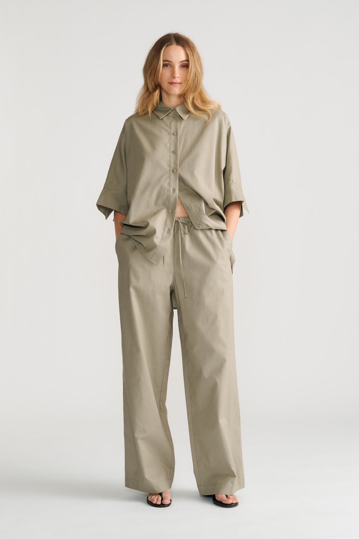 Woman wearing relaxed fit olive green pants with a matching oversized button-up shirt and black sandals.