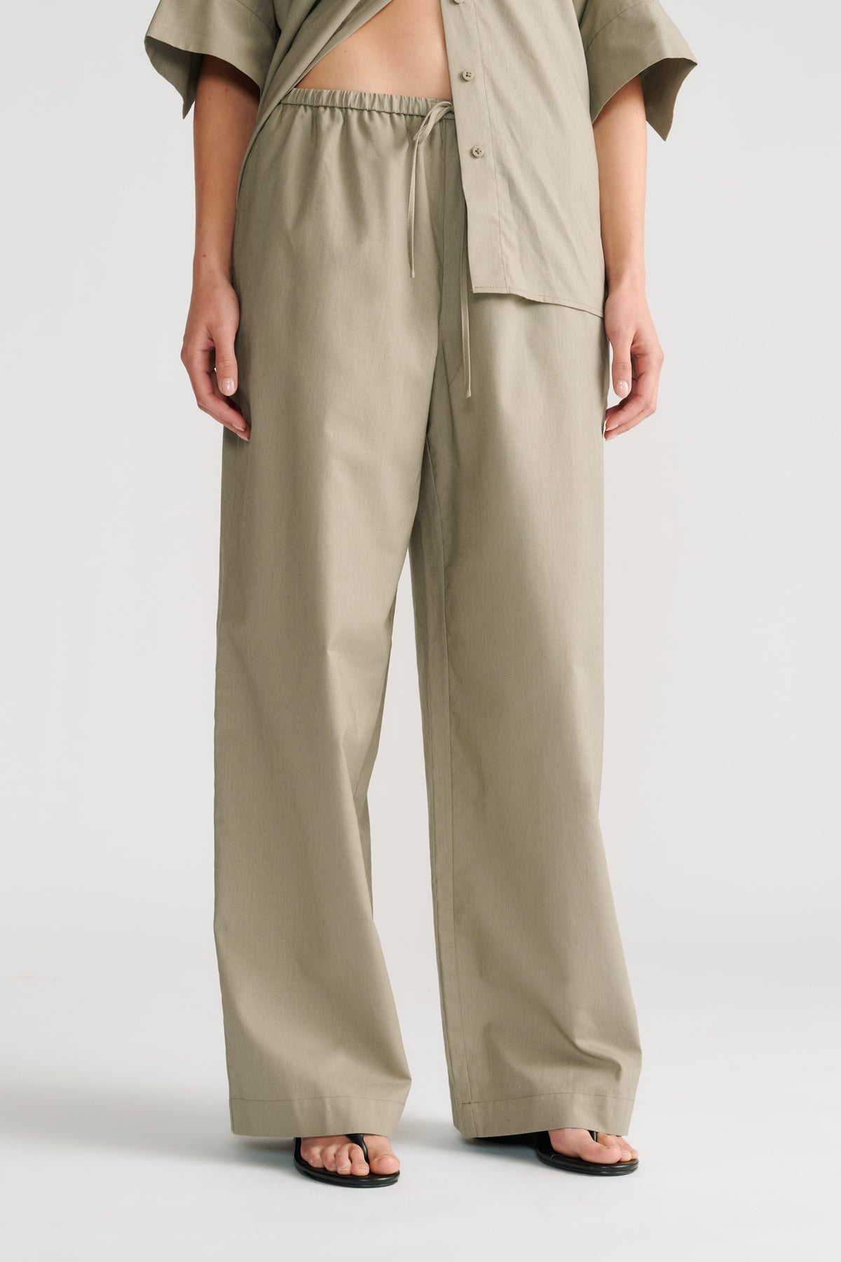 Woman wearing relaxed sage green pull-on wide-leg pants with a matching open shirt and black sandals.