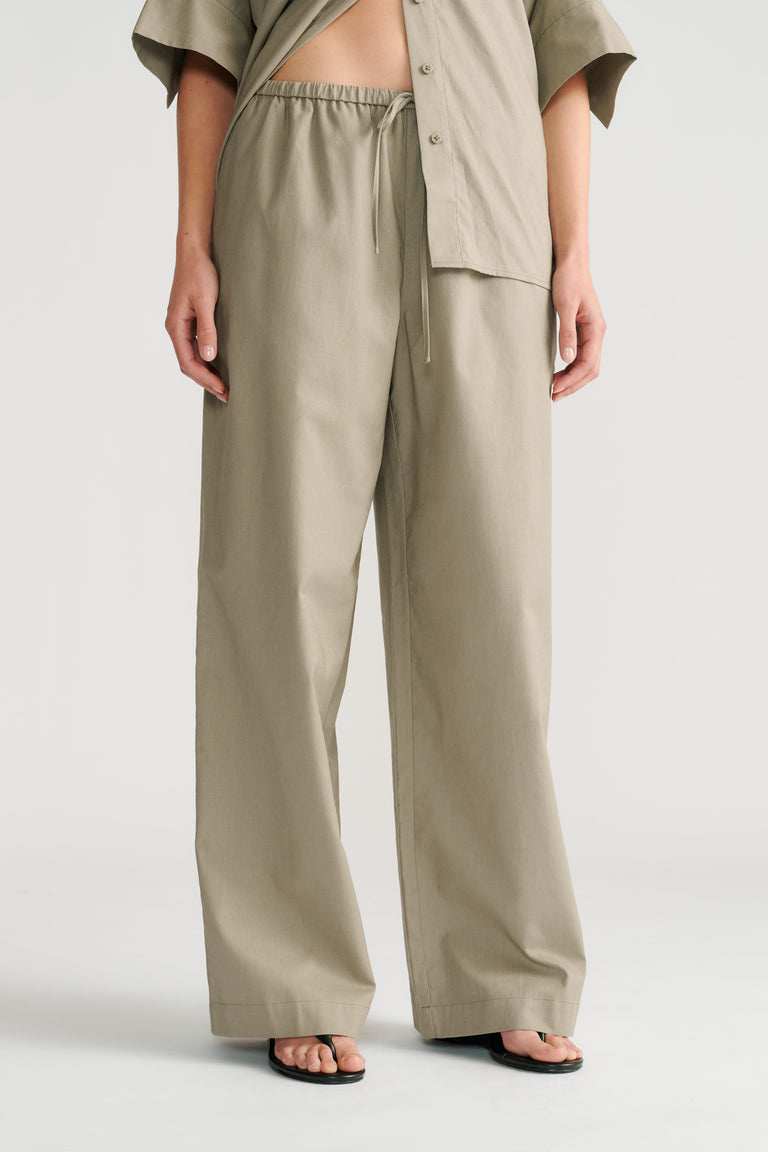 Woman wearing relaxed sage green pull-on wide-leg pants with a matching open shirt and black sandals.
