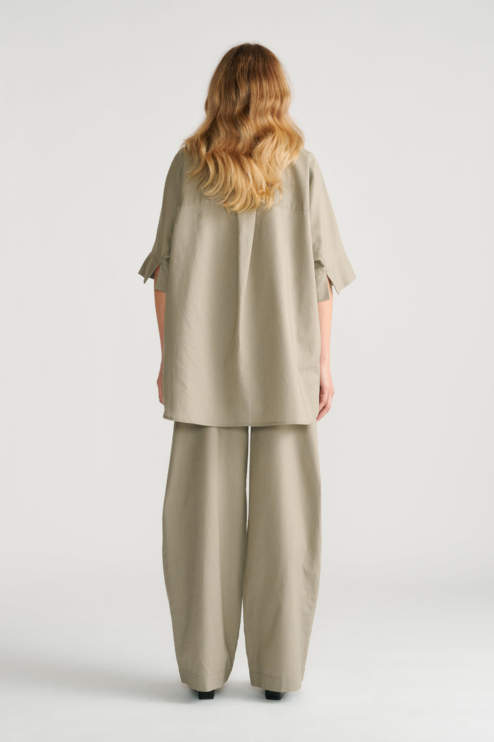 Woman seen from behind wearing sage green relaxed wide-leg pants with a loose matching tunic top.