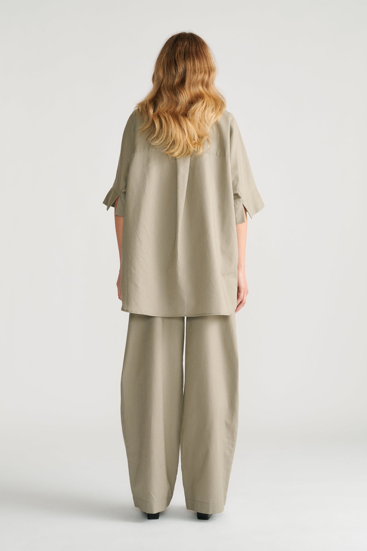 Woman seen from behind wearing sage green relaxed wide-leg pants with a loose matching tunic top.