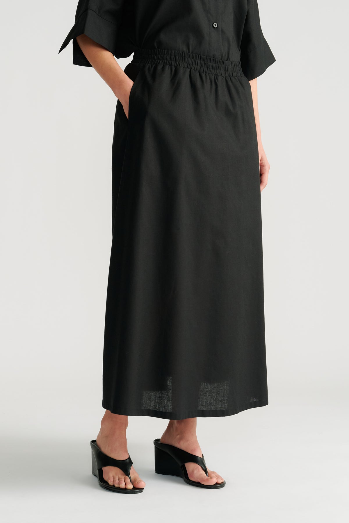 Woman wearing a black midi skirt with an elastic waistband paired with black wedge sandals and a relaxed black top